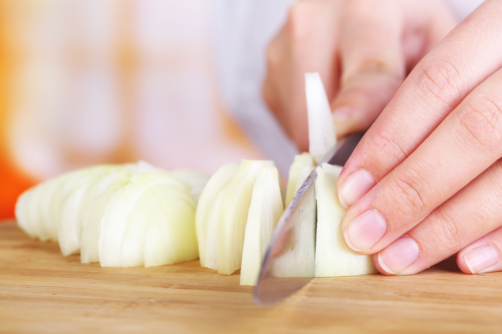 Female hands cutting bulb onion, on kitchen background