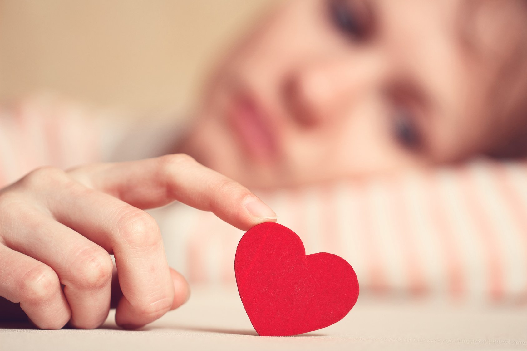 Sad girl is holding heart symbol by her finger