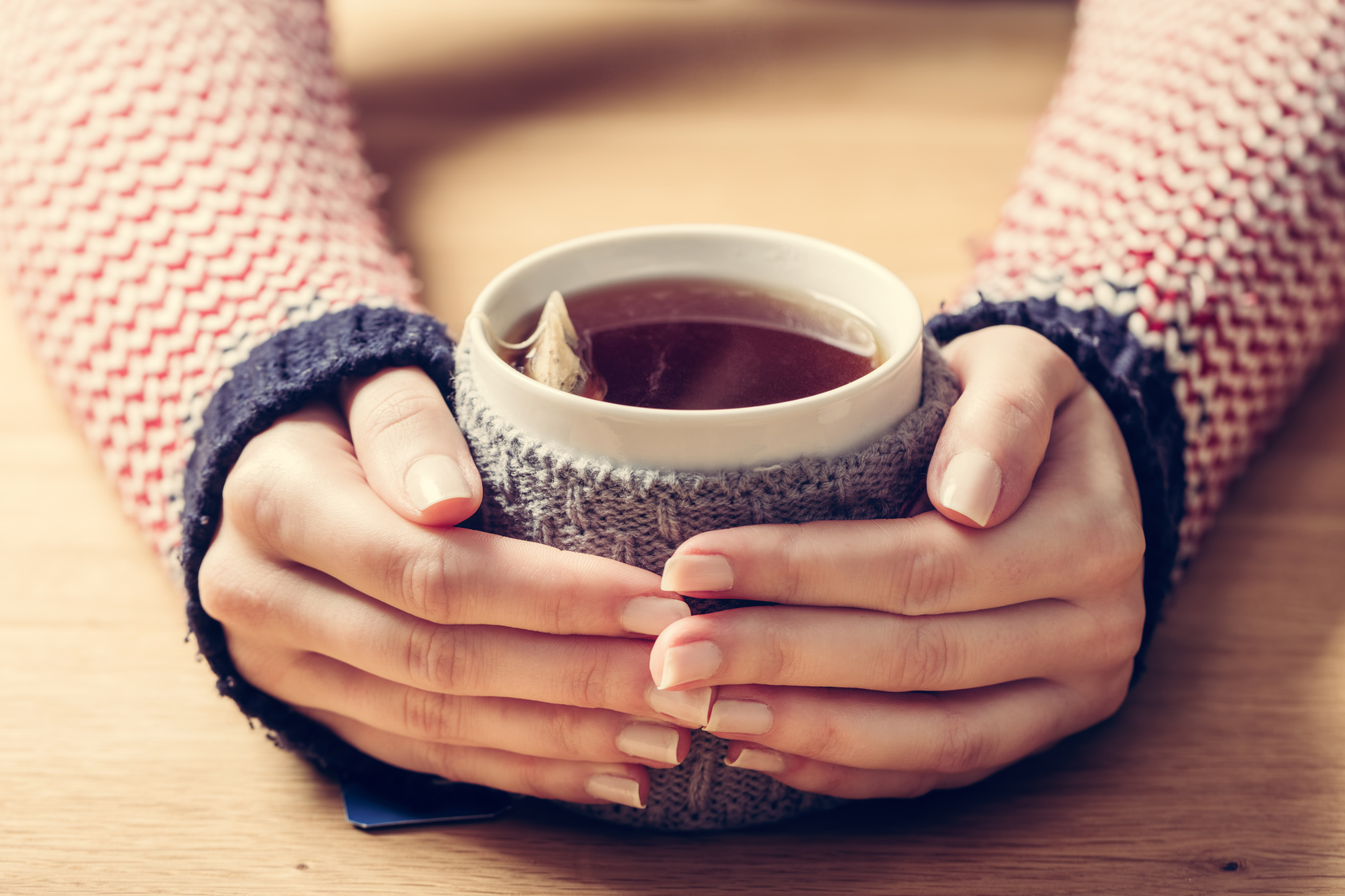 Hot mug of tea warming woman’s hands in retro jumper.