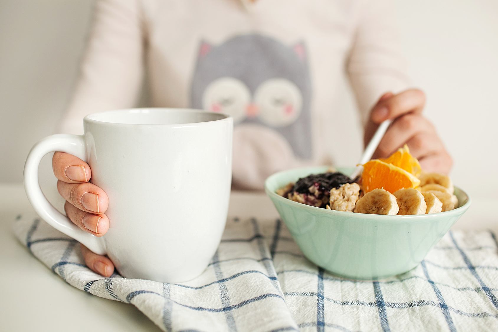 Woman holds tea cup and spoon with porridge and fruits