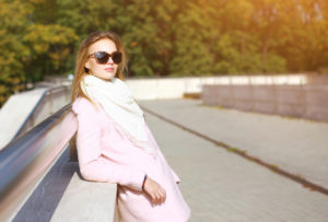 Fashionable woman in white coat and sunglasses in the city