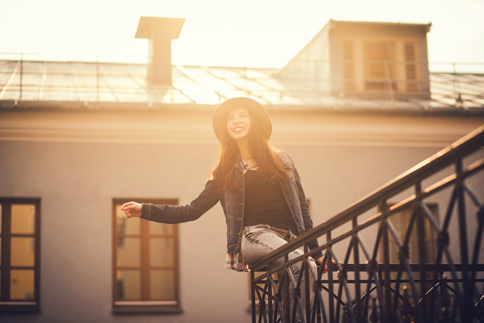 sunny portrait of a happy girl sitting on the railing at sunset