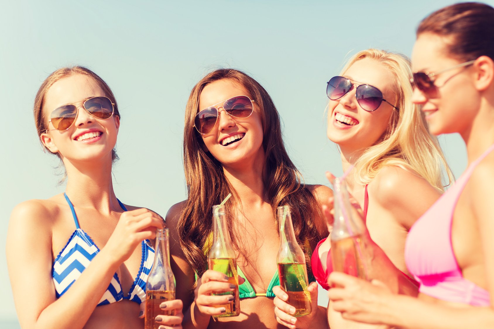 group of smiling young women drinking on beach
