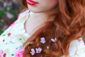 portrait of beautiful woman near the cherry blossom branch. Purple flowers in red hair. Lips.