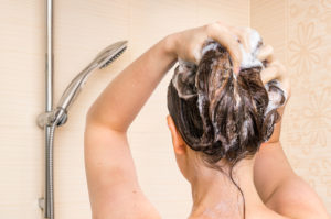 Attractive woman washing her hair with shampoo in shower