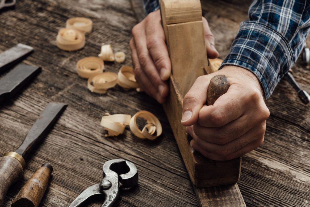 Carpenter working in his workshop, he is smoothing a wooden board using a planer, carpentry, carpentry, woodworking and craftsmanship concept