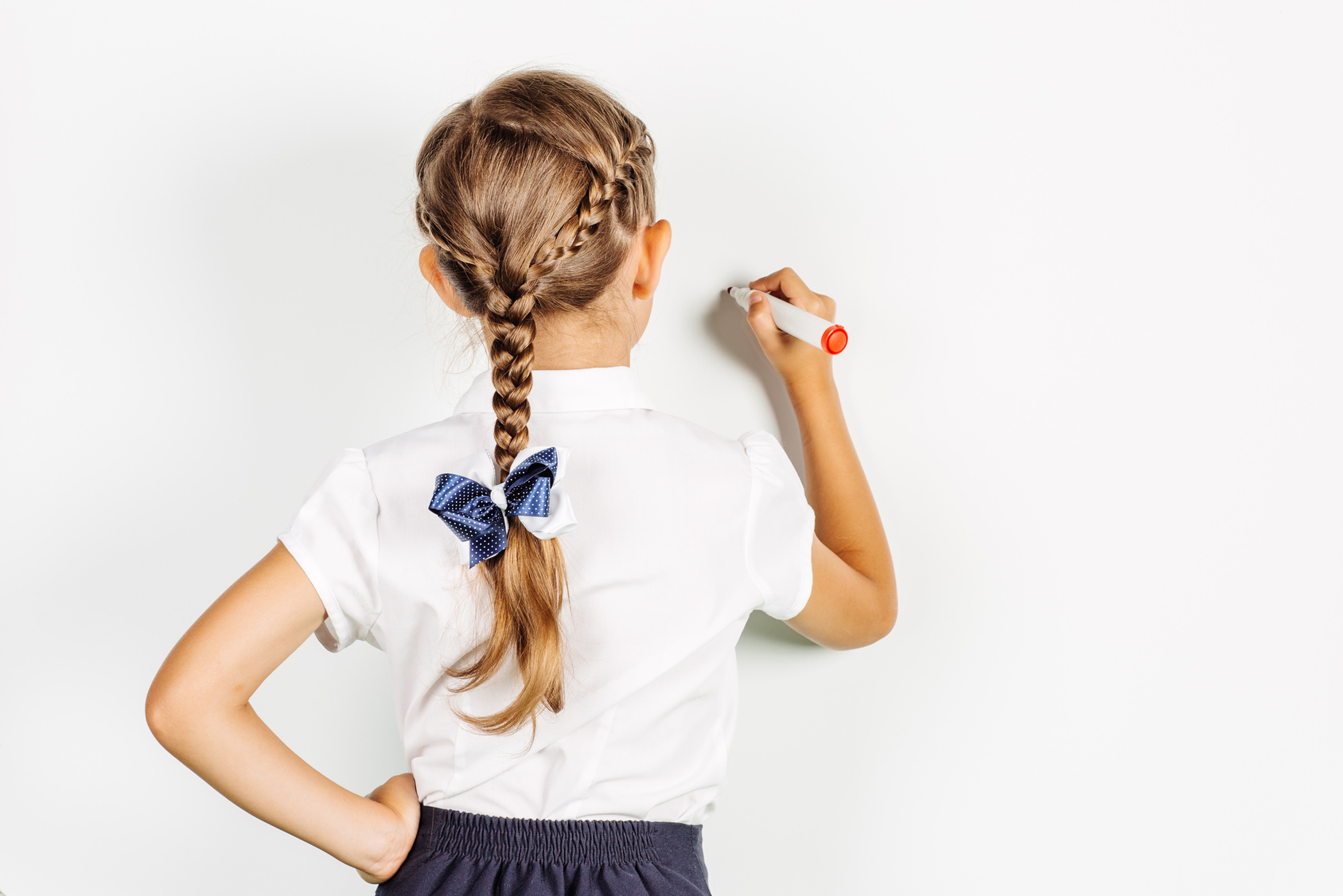 school girl in a school uniform writing something on board