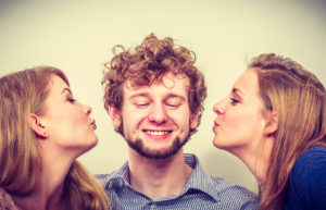 Two pretty young women kissing handsome man.