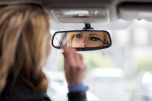 Beautiful young woman applying make-up while driving car