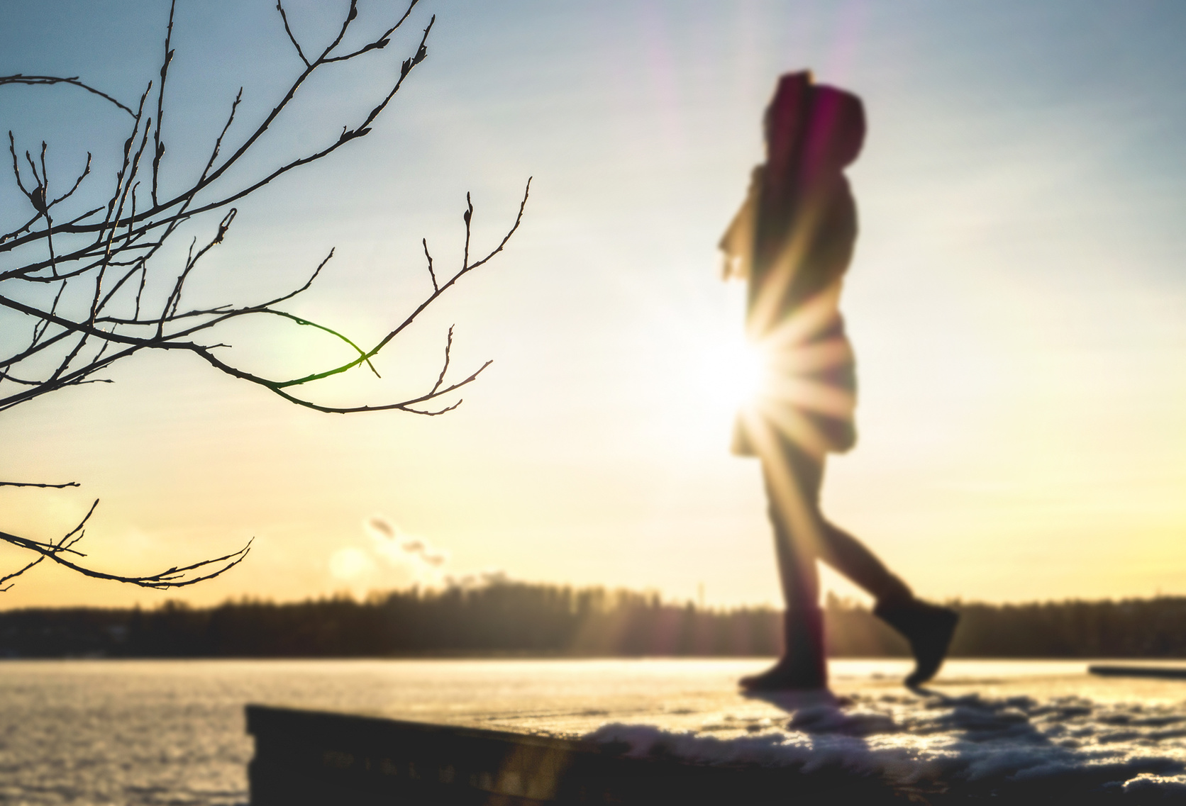 Woman standing on a pier by a lake in winter at sunset. Silhouette girl with snow and ice. Trendy cold weather clothes and fashion.
