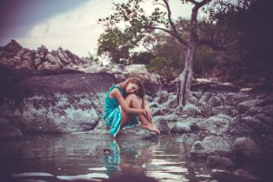 Young beautiful woman in long turquoise dress sitting on a stone by the sea. Retro colors