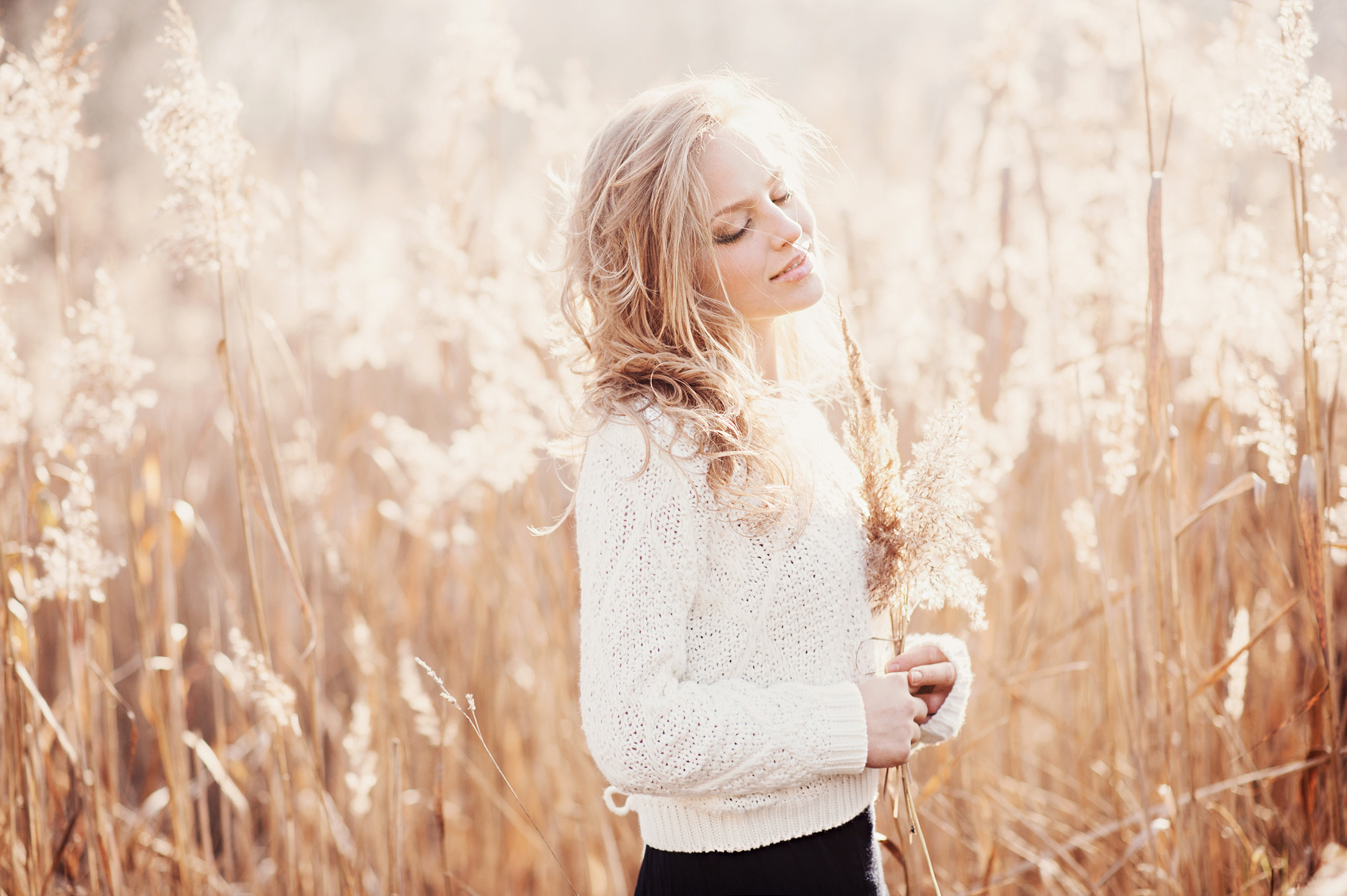 Portrait of a beautiful young blonde girl in a field in white pullover, smiling with eyes closed, concept beauty and health