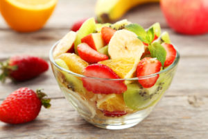 Fresh fruit salad in bowl on grey wooden background