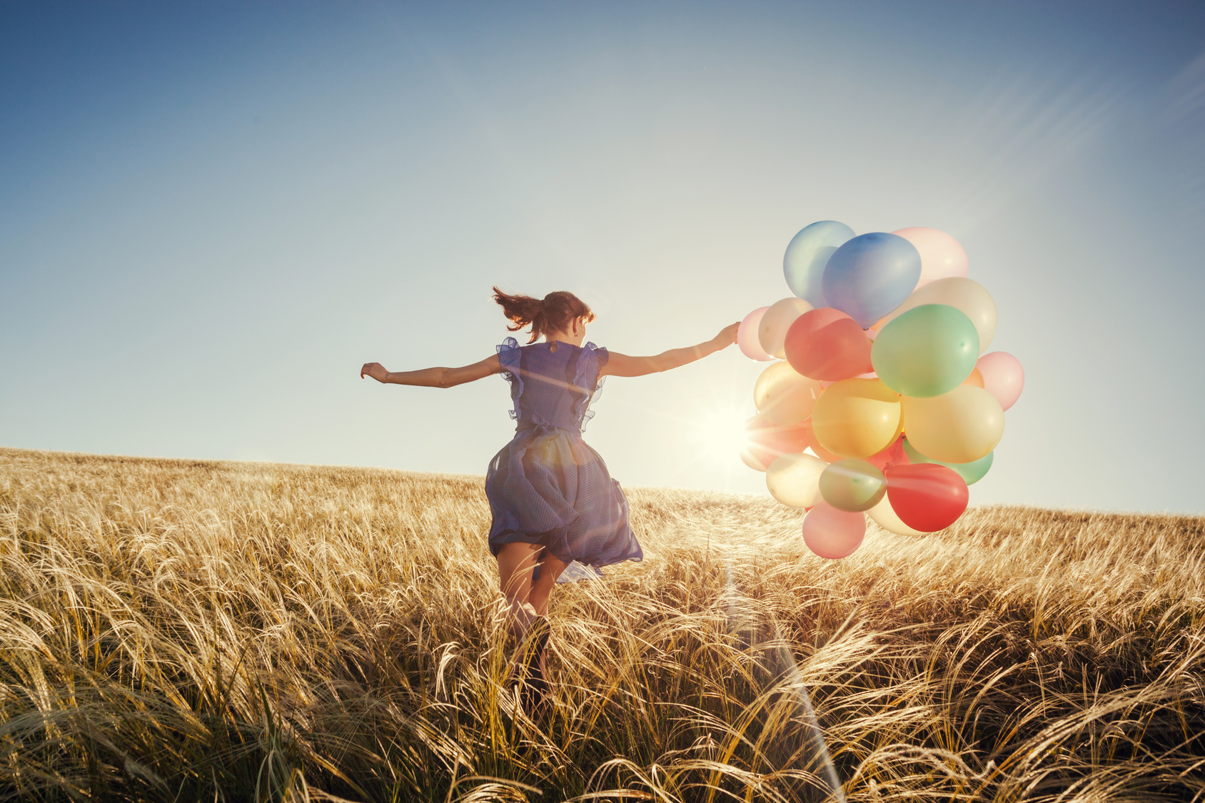 Girl running on field with balloons at sunset. Happy woman retro