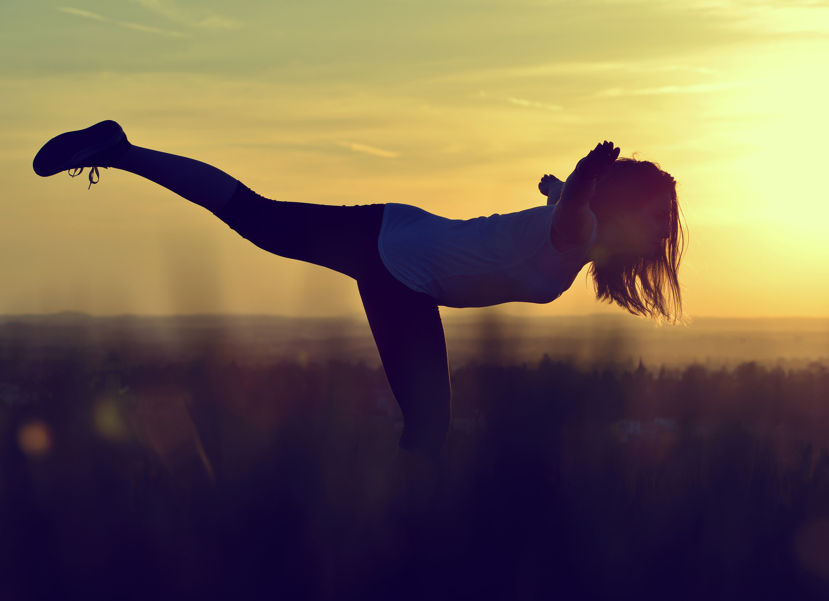 Silhouette of young woman stretching on a meadow at sunset