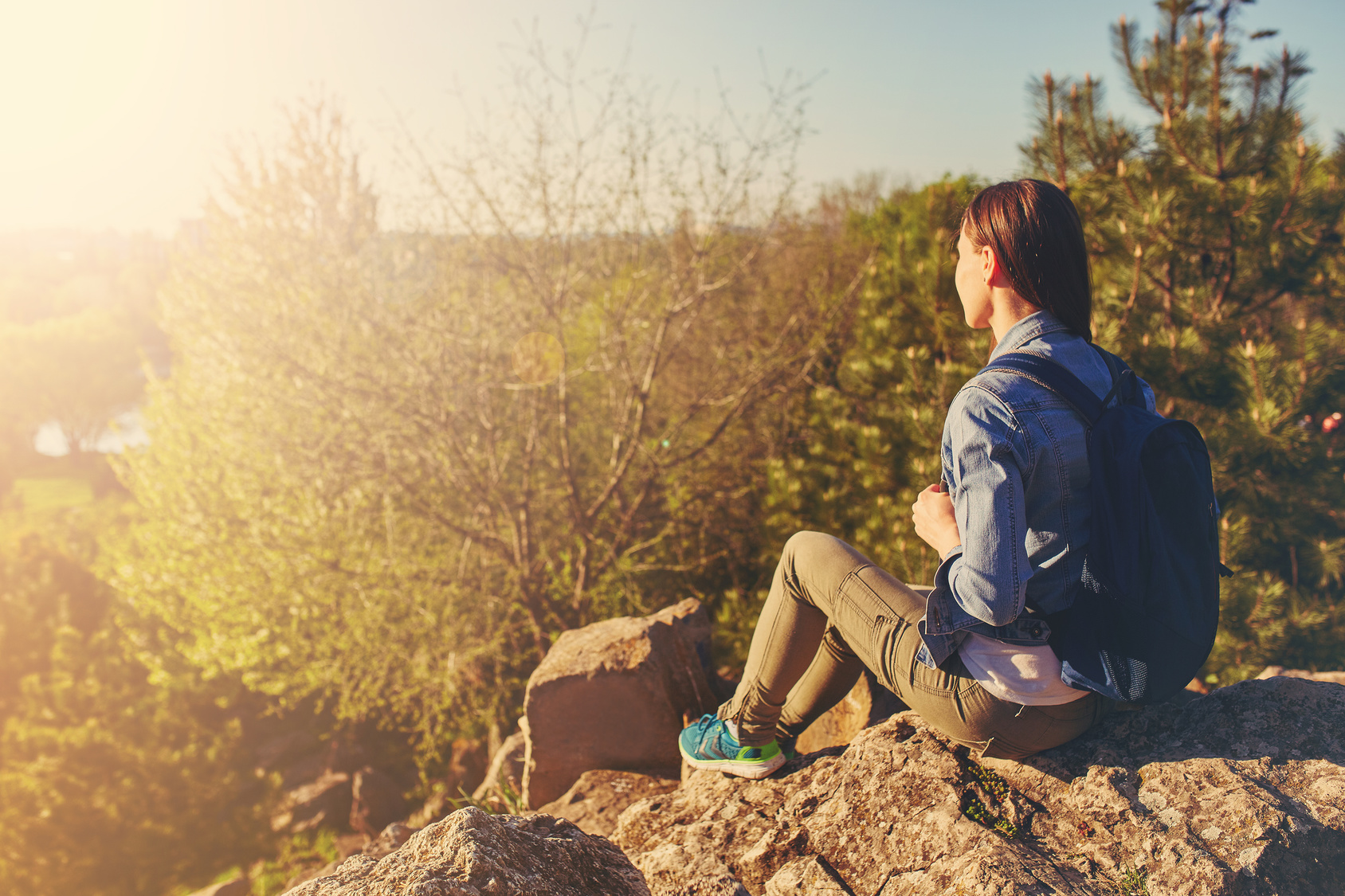 Young woman with backpack sitting on cliff