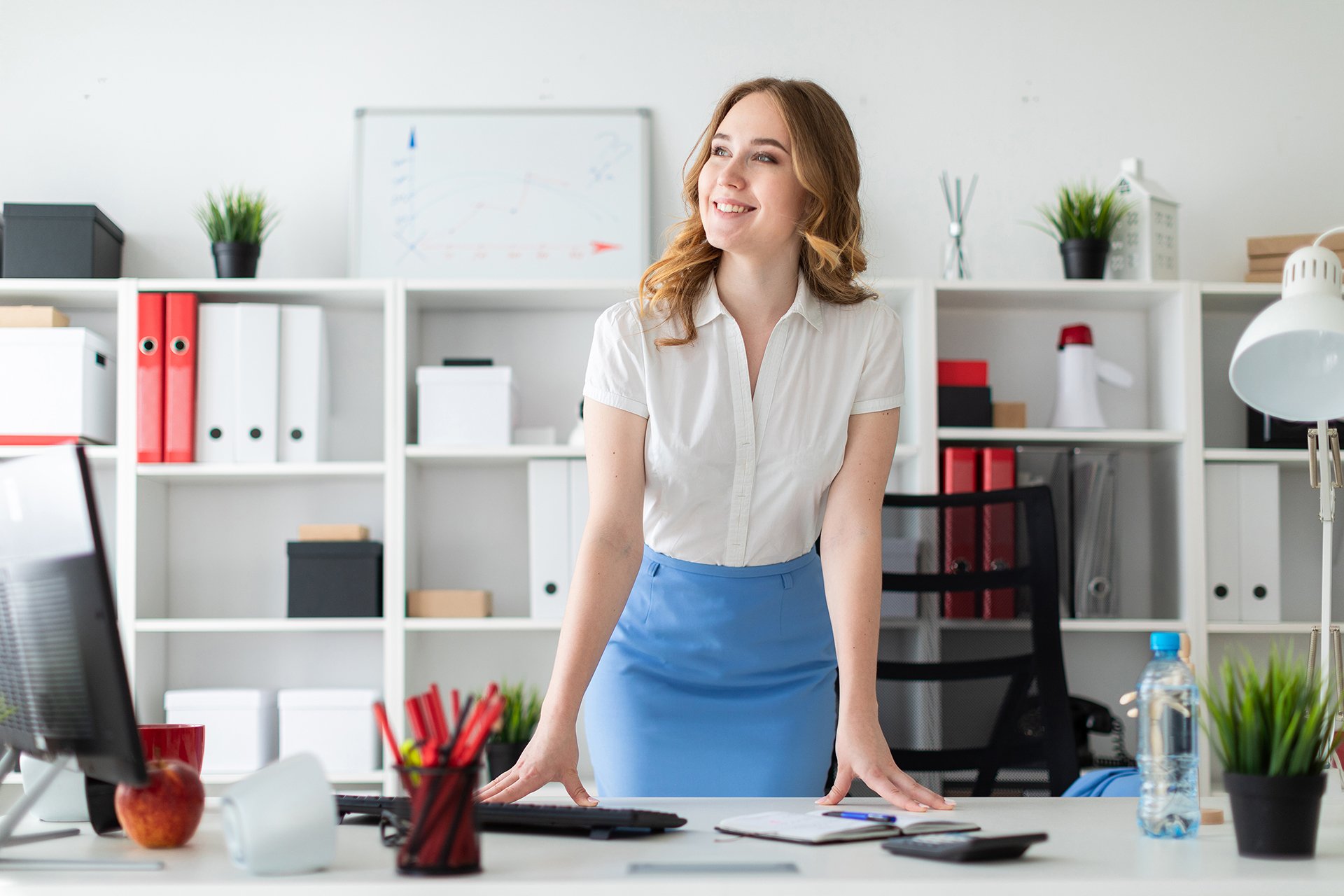 A beautiful young girl stands in the office, hands on the table.