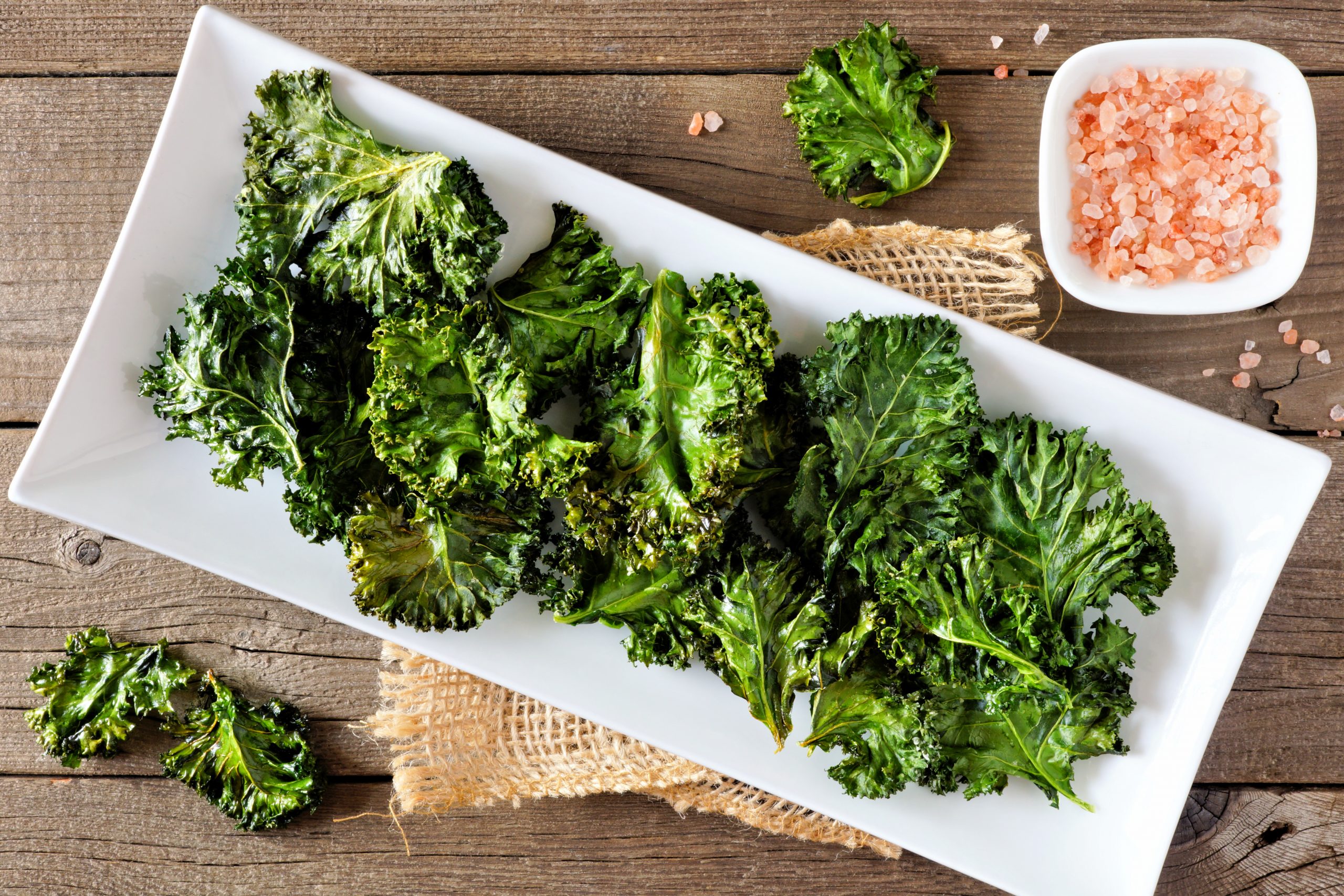 Plate of healthy organic kale chips, top view on rustic a wood background