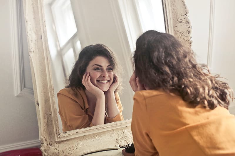 young-woman-in-yellow-collared-shirt-looking-herself-reflection-in-mirror-at-home