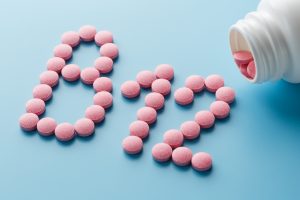 Pink round vitamins B12 shaped pills on a blue background spilled from a white can