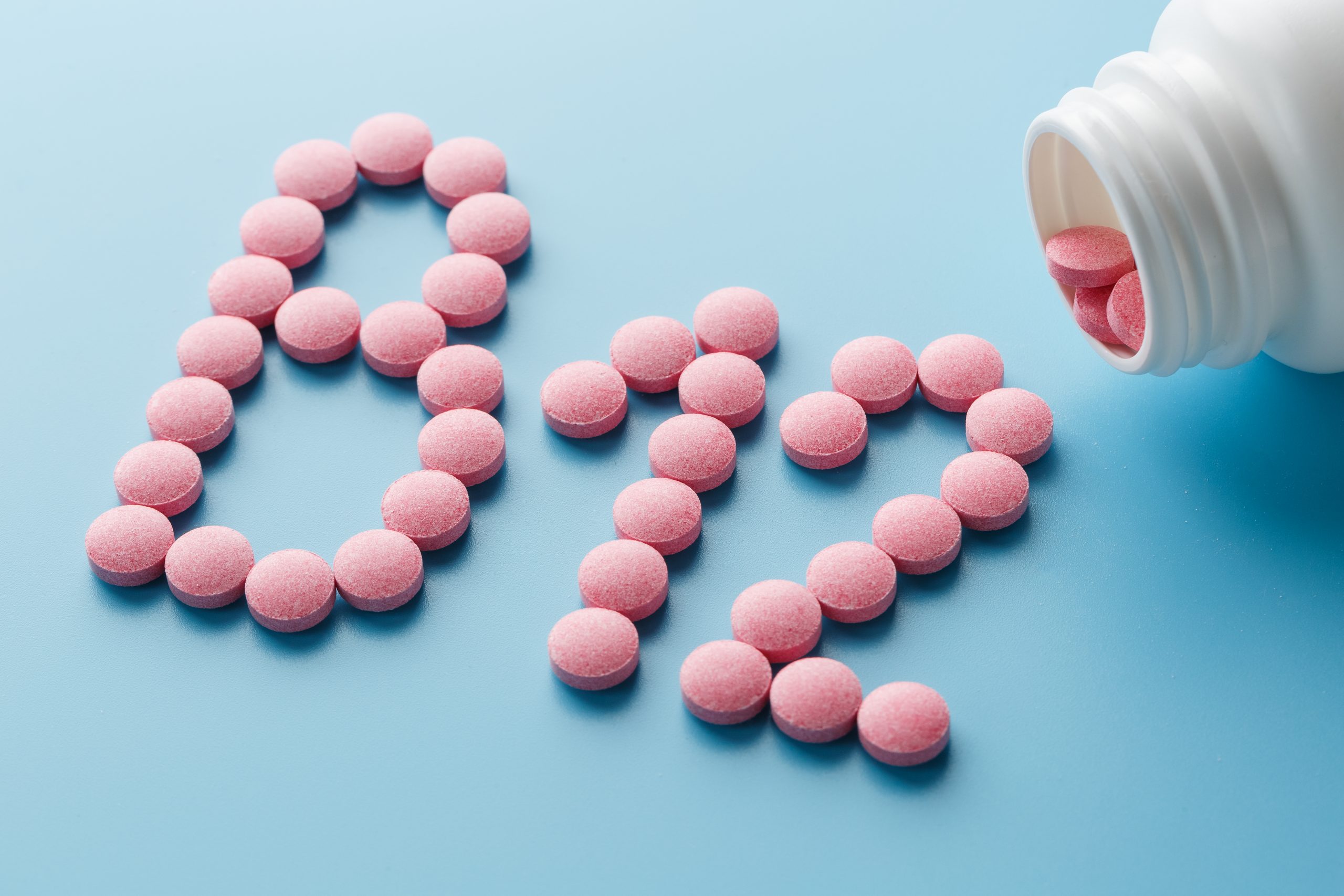 Pink round vitamins B12 shaped pills on a blue background spilled from a white can