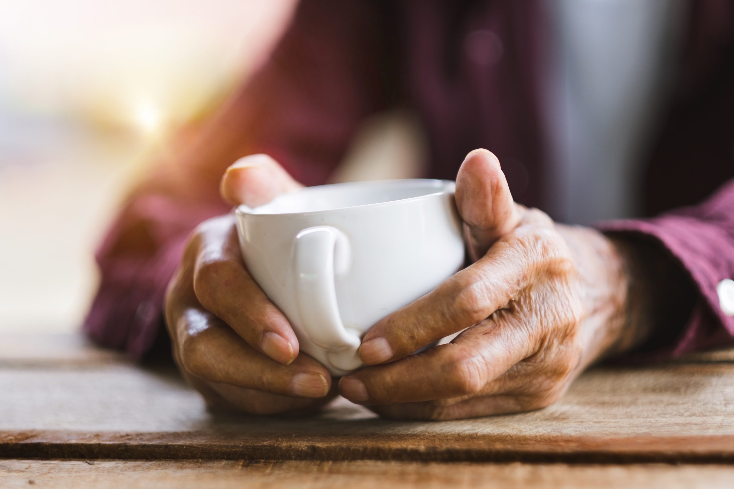 Hands of old man holding cup of coffee on the wood table.vintage tone