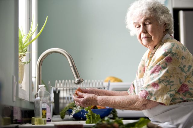 Old woman in kitchen pictured while washing carrots and radishes