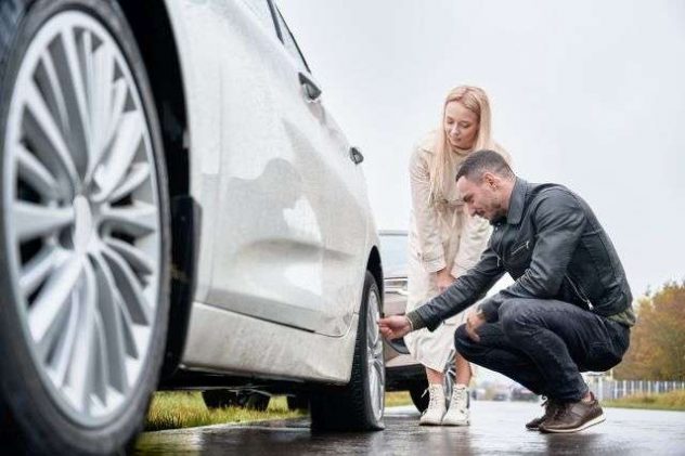 young-man-helping-charming-woman-fix-car-wheel